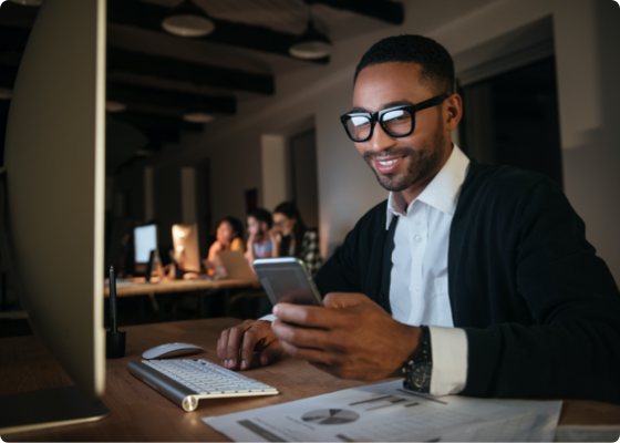 Homem no espaço de trabalho a olhar para o seu telemóvel com um sorriso