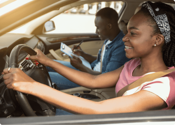 Instructor del DMV y una joven conduciendo y sonriendo