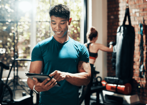 A smiling man tapping to his tablet in a gym