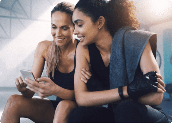 Zwei Frauen sitzen in einem Fitnessstudio mit einem Handy
