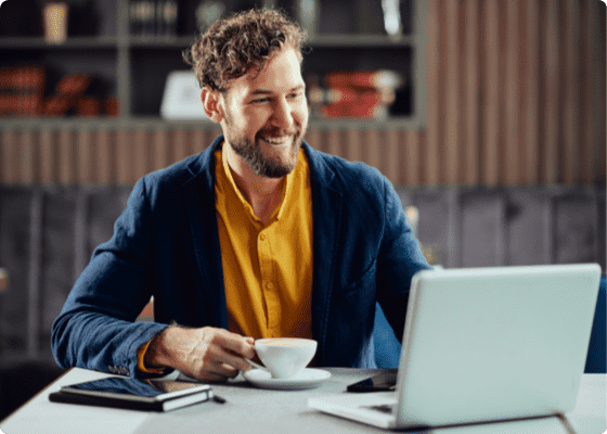 A man in blue jacket looking to laptop with coffee