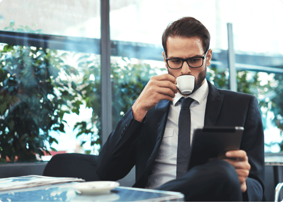 Um homem olha para o seu tablet enquanto bebe café