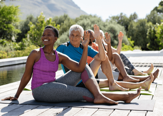 cuatro personas sentadas al aire libre en el suelo en postura de yoga