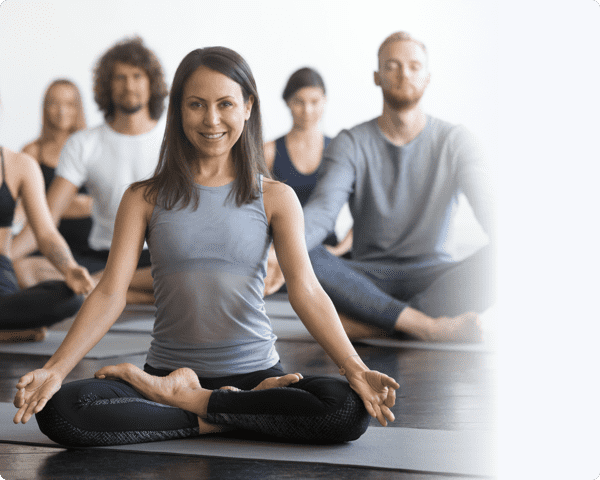 Uma mulher de top cinzento a liderar alguma pessoas num salão de ioga