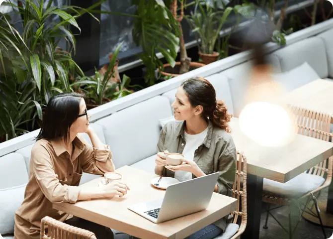 Two women sitting outdoor with a laptop and coffee