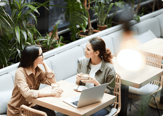 Zwei Frauen sitzen draußen mit einem Laptop und Kaffee