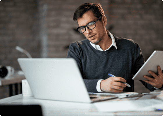 Un uomo seduto che lavora con un tablet e un laptop